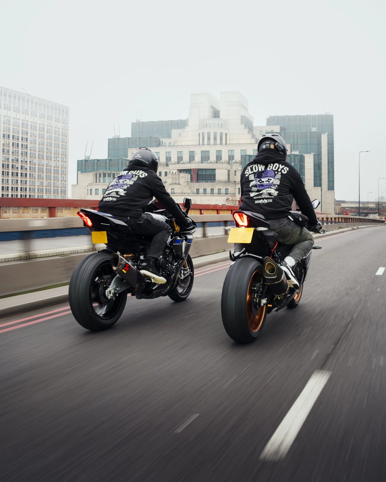 Two Slowboys members riding together across a city bridge